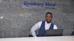 A reception desk at the Residency Hotel with a marble wall background and a sign that reads "Residency Hotel Welcome Home." - Residency Hotel Lekki Lagos (Lekki)