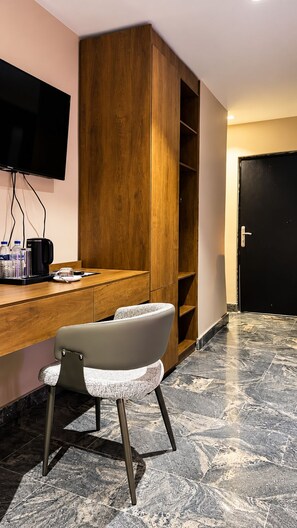A hotel room with a wooden desk, a flat-screen TV mounted on the wall, a modern chair, and a marble-patterned floor. - Residency Hotel Lekki Lagos (Lekki)
