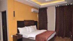 A hotel room with a bed, bedside table, and a small table with a remote control. - Residency Hotel Lekki Lagos (Lekki)