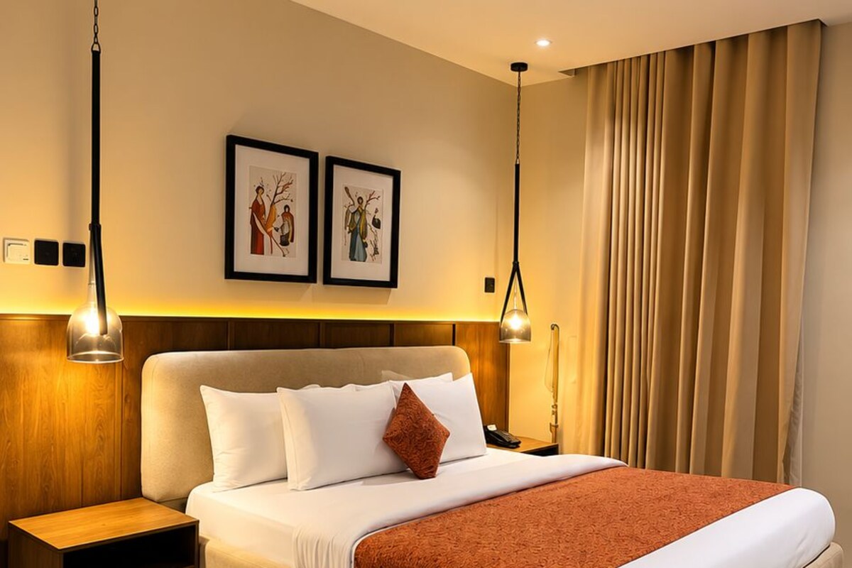 A modern hotel room with a large bed, bedside tables, a nightstand, and two wall-mounted lamps.