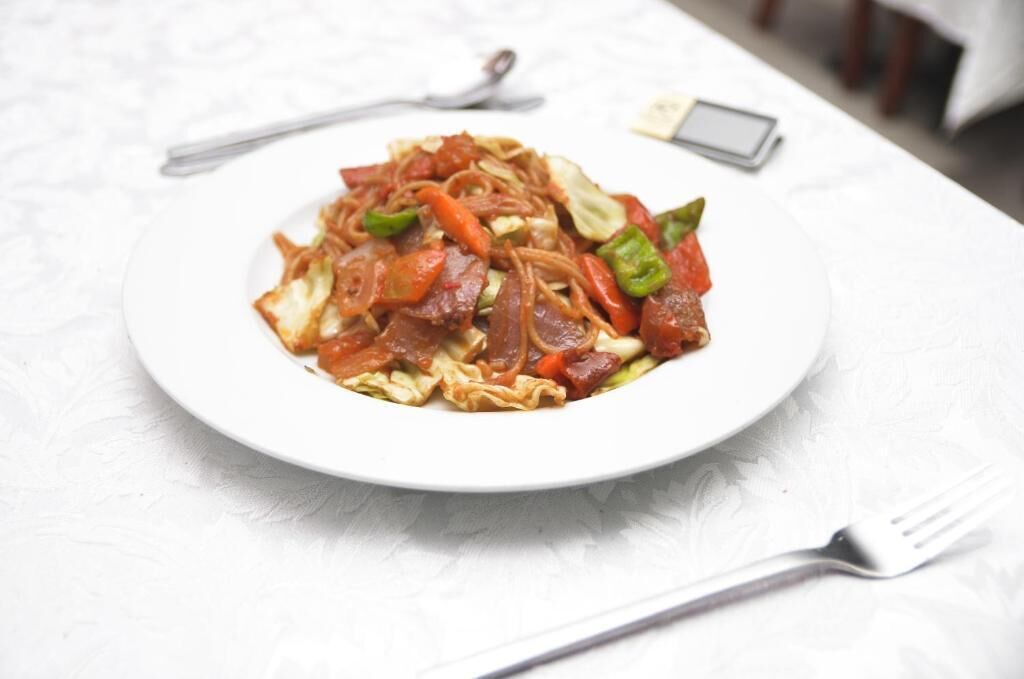 Un plato de fideos salteados con verduras y carne sobre un mantel blanco.
