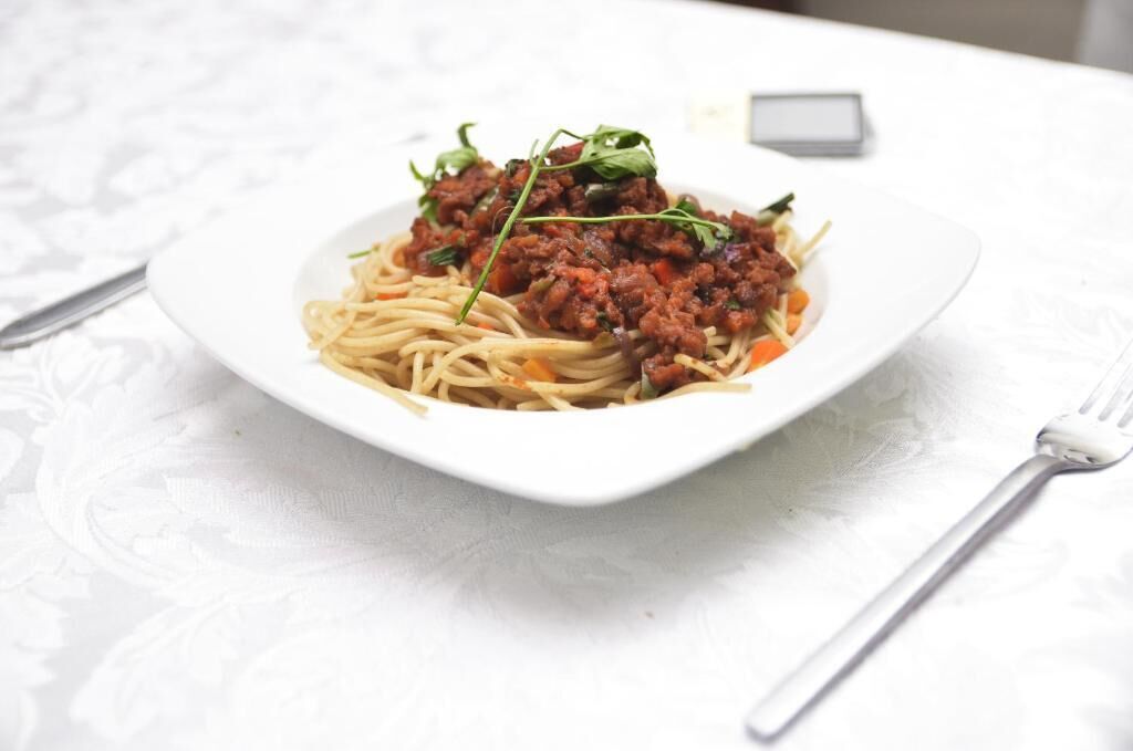 A plate of spaghetti with a meat sauce and garnish on a white tablecloth.