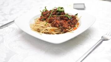 A plate of spaghetti with a meat sauce and garnish on a white tablecloth.