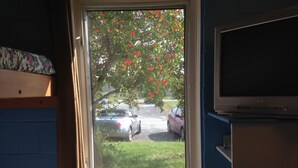 A room with a window overlooking a parking area and a tree with red flowers. - Motel Econo-Nuit (Sherbrooke)