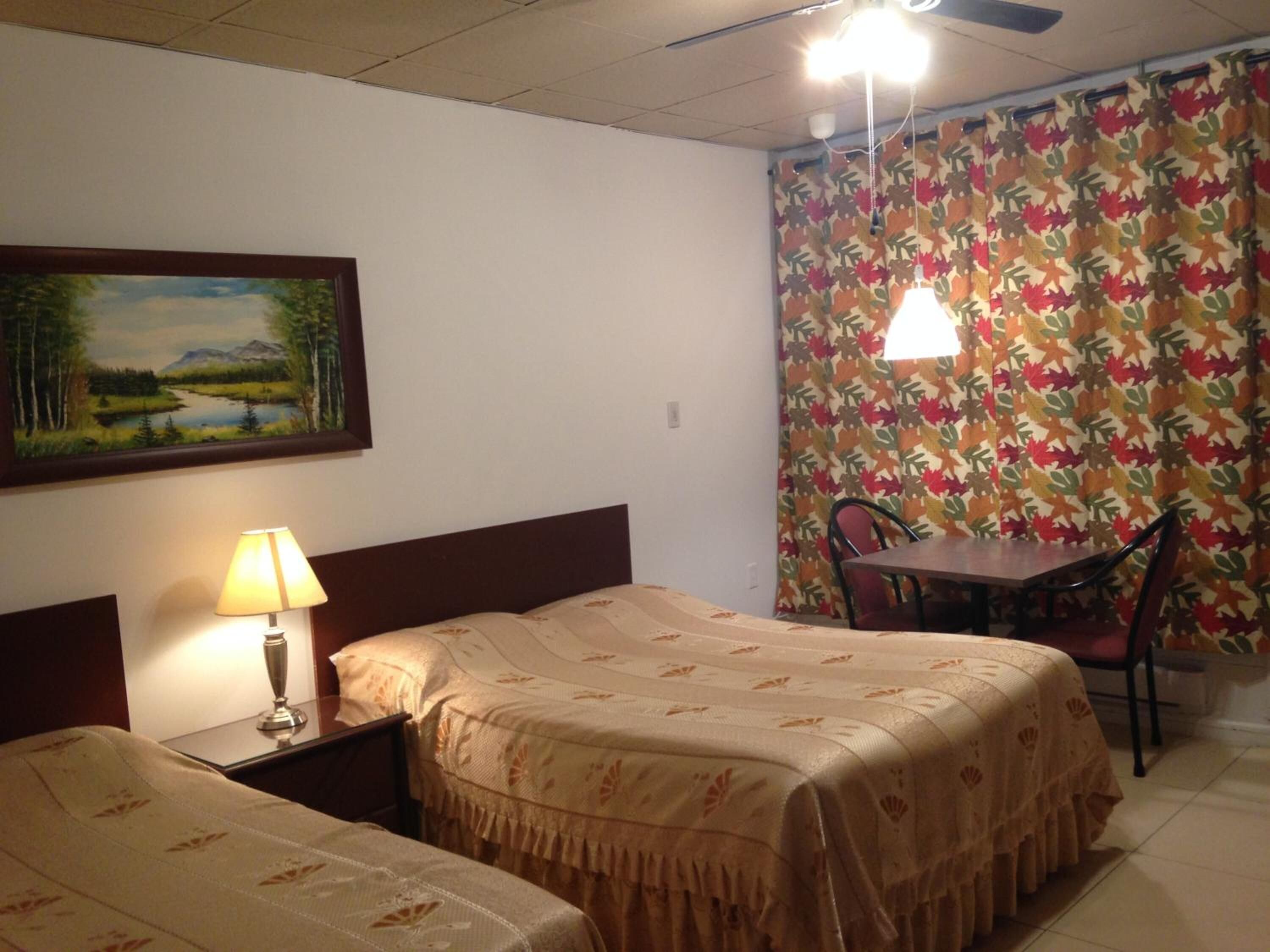 Habitación de hotel con dos camas, un cuadro de un paisaje, una mesa con sillas y una cortina con estampado de hojas.