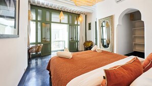 Une chambre d’hôtel avec un grand lit, une chaise, un miroir et un balcon avec vue.