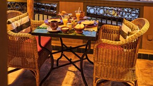 Un espace de restauration en plein air, avec des chaises en osier et une table dressée pour deux, offrant une vue sur un paysage urbain ponctué de palmiers et d’immeubles.