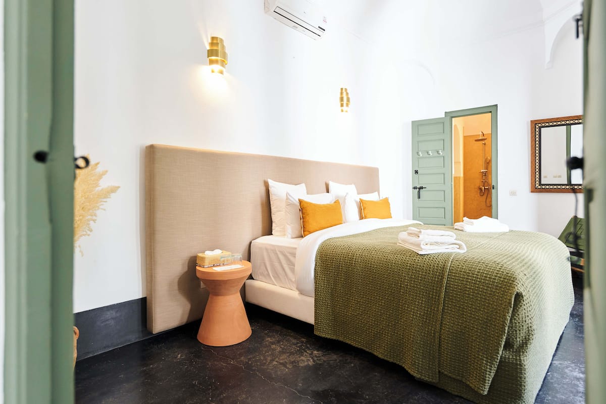 A hotel room with a bed, a small side table, a green door, and a mirror on the wall.