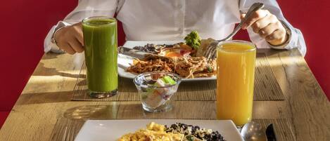 Une table à manger avec un repas composé d’œufs brouillés, de haricots noirs, de riz et d’une tortilla garnie. On y trouve également deux boissons, une verte et une orange.