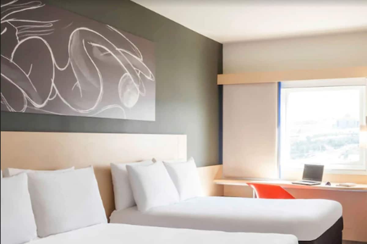 A hotel room with two beds, a desk with a laptop, and a large window.