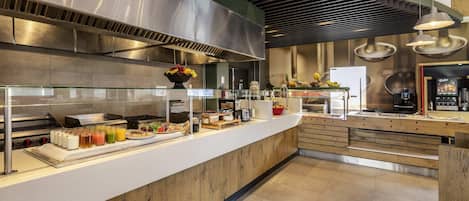 Una barra de desayuno moderna con una campana extractora de acero inoxidable, una exposición de frutas y una máquina de café.