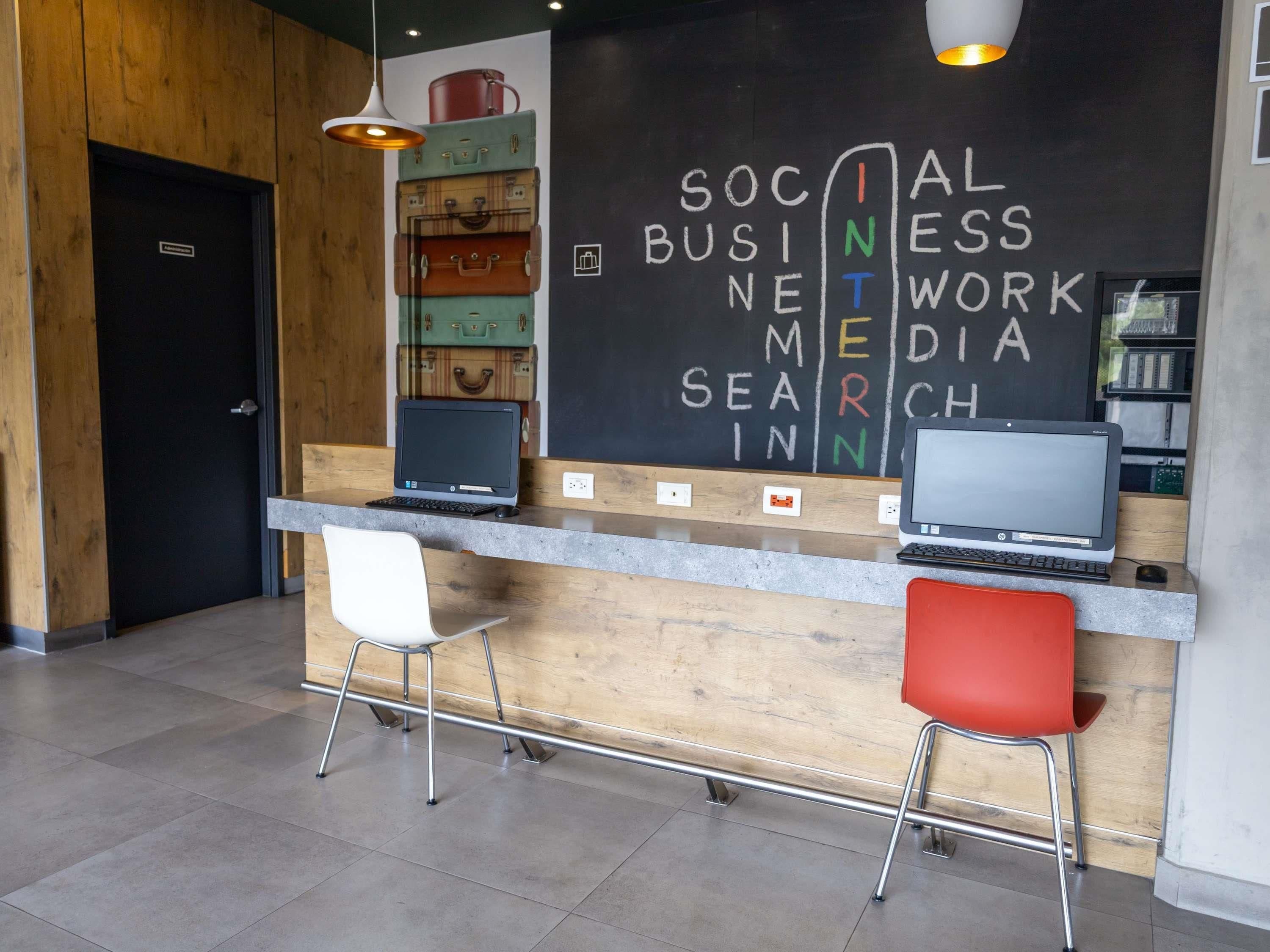 A reception desk with two laptops, a white chair, a red chair, and a wall with chalkboard writing.