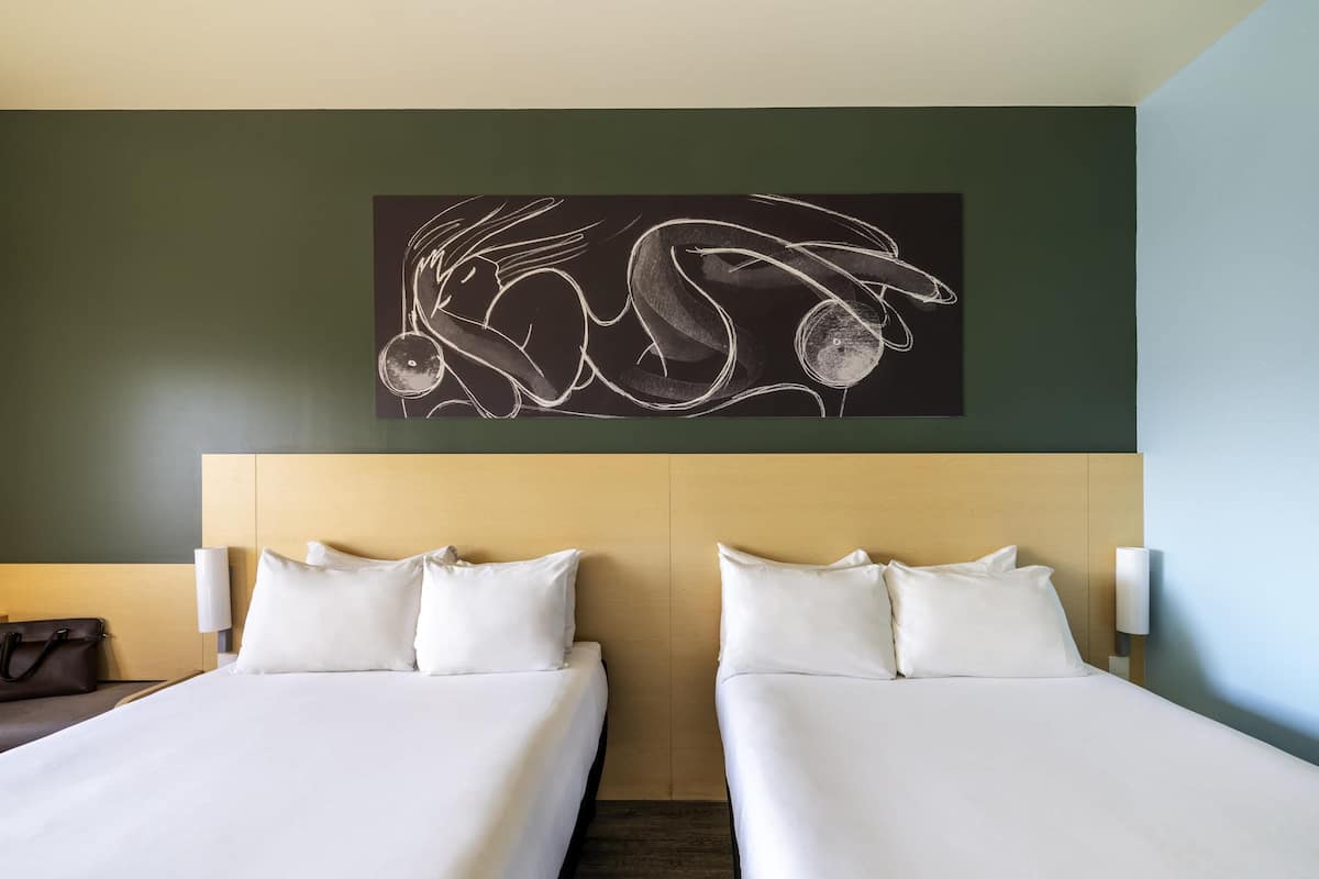 A hotel room with two beds, a dark wall with a chalkboard drawing, and a wooden headboard.