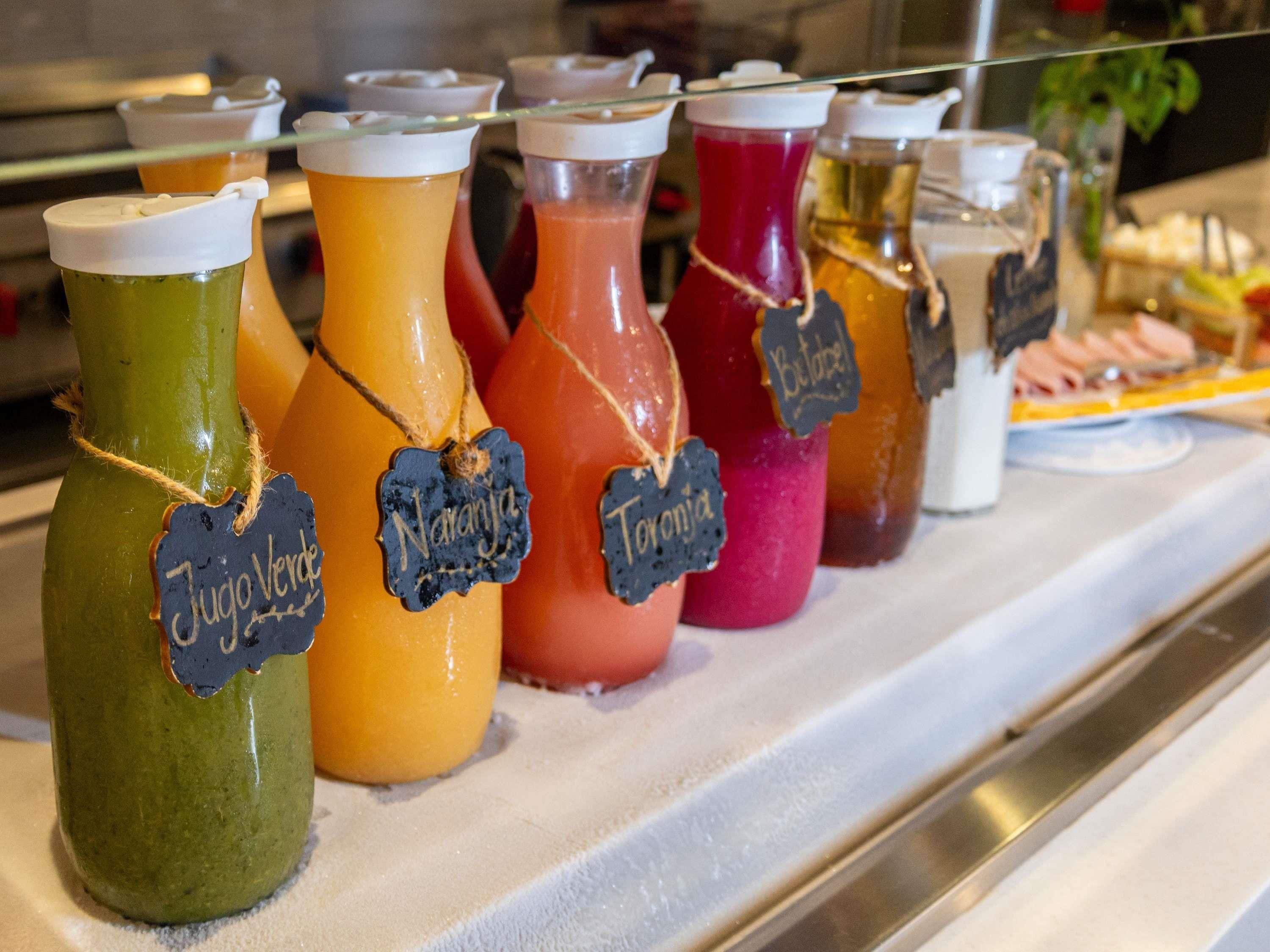 A variety of colorful beverages in glass bottles with labels, displayed on a counter.