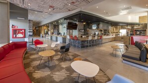 A modern interior with a curved red sofa, round tables, and a kitchen area with a bar. - ibis Queretaro (Querétaro)