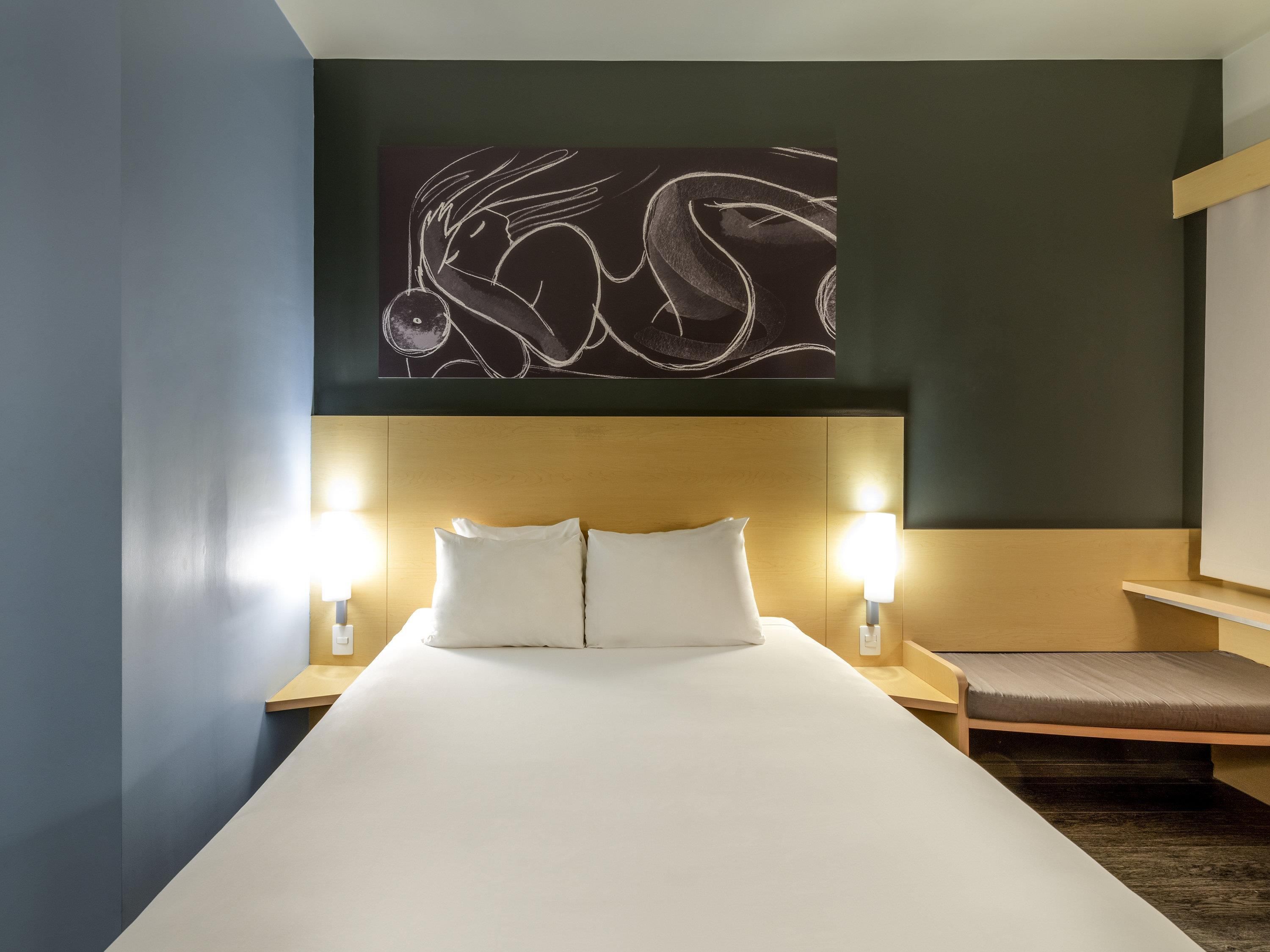 Una habitación de hotel con una cama grande, dos lámparas de noche, un cabecero de madera y una obra de arte en la pared sobre la cama.