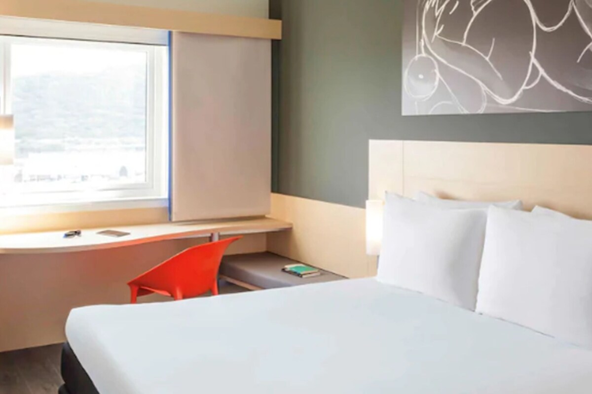 A hotel room with a bed, a desk, a chair, and a window.
