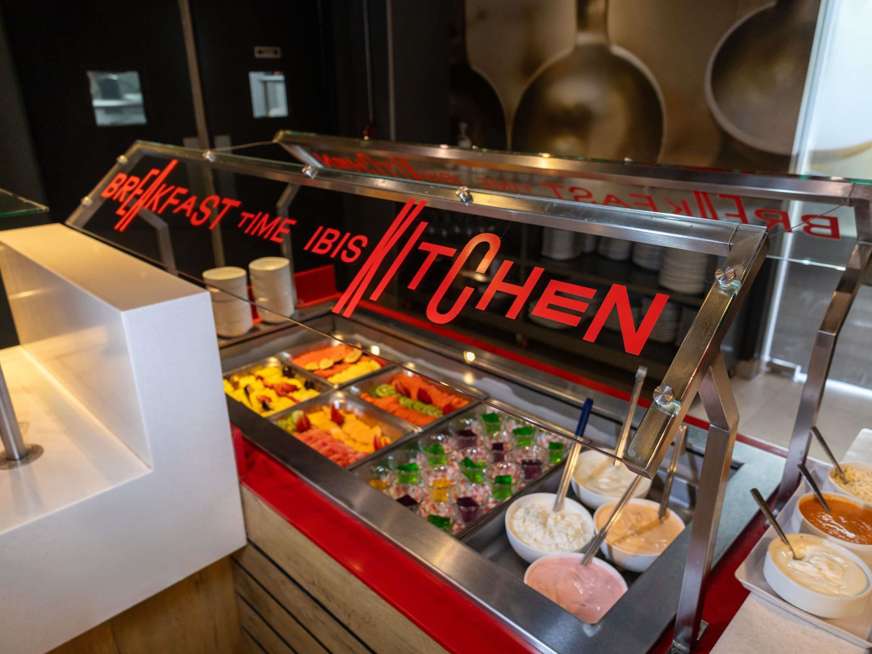A breakfast buffet counter with various food options and a sign that reads 'BREAKFAST TIME IBIS KITCHEN'.