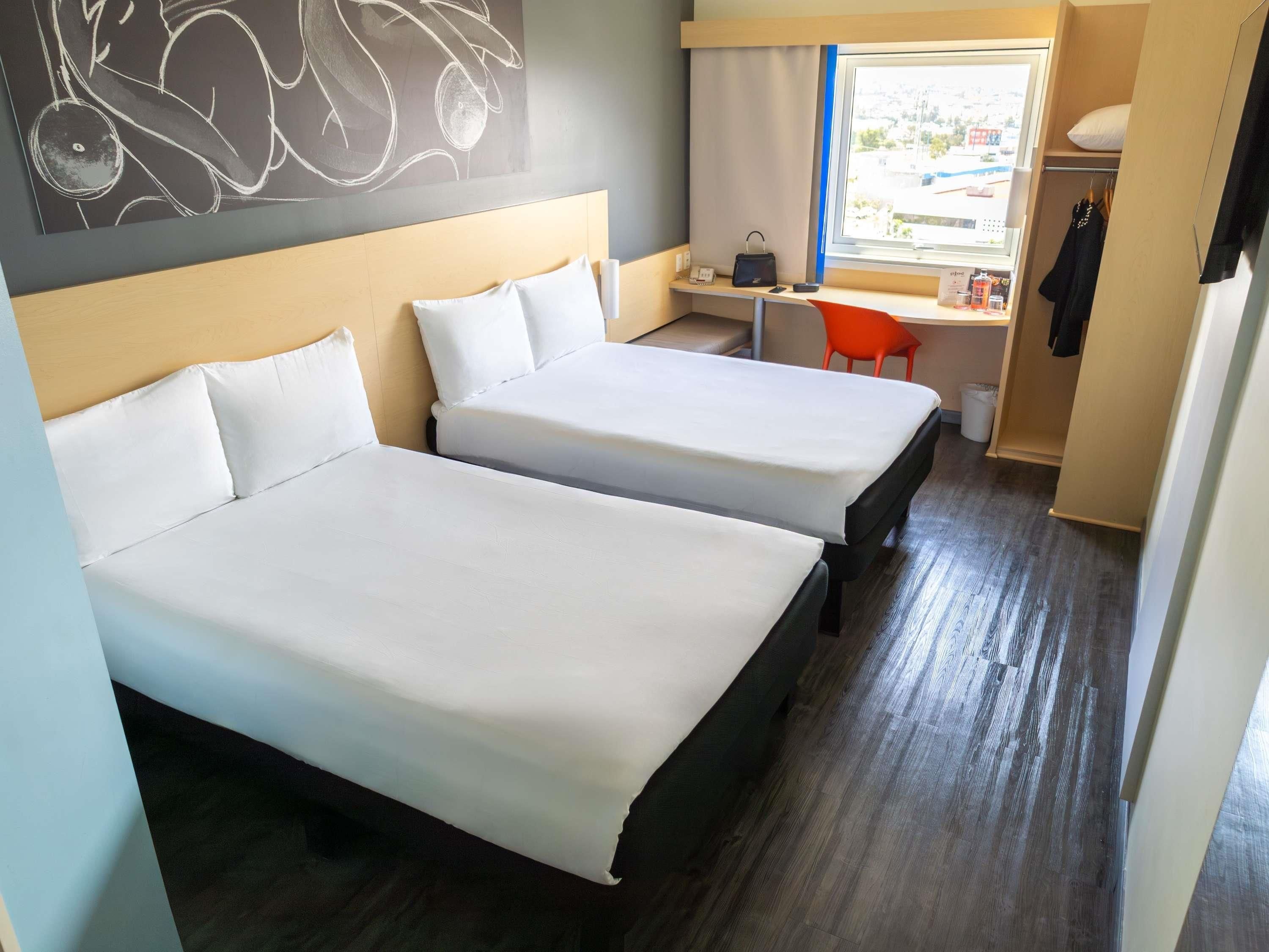 Habitación de hotel con dos camas, un escritorio, una silla y ventana con vistas.