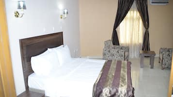 A hotel room with a bed, two chairs, a small table, and a window with curtains.
