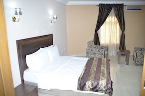 Una habitación de hotel con una cama, dos sillas, una mesita y un ventanal con cortinas.