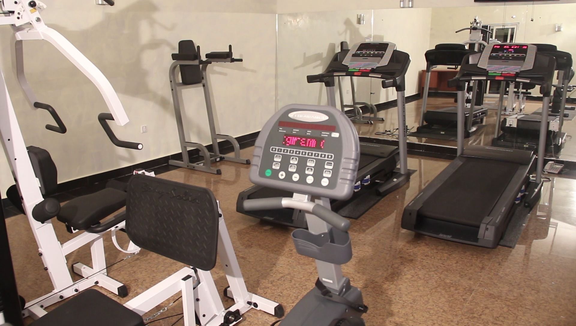 A gym with various exercise equipment including treadmills, a weight machine, and a bench.