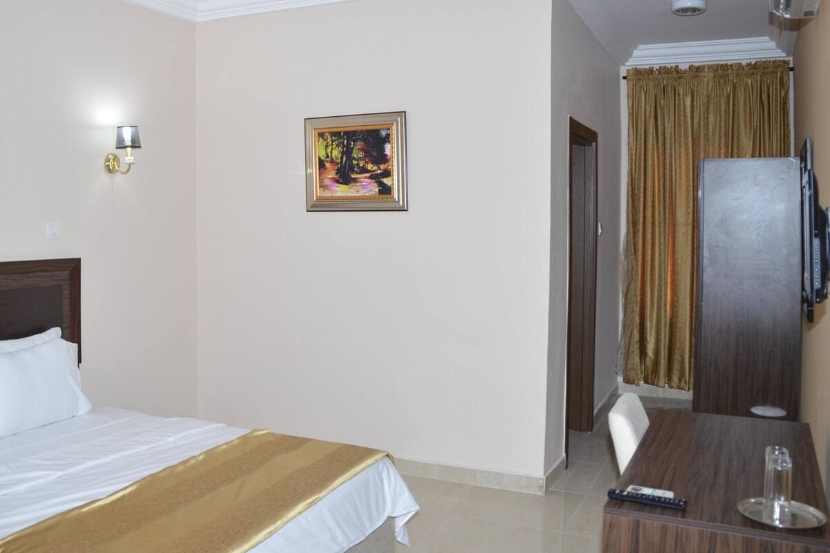 A hotel room with a bed, a painting, a television, and a dining table.