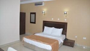 A bedroom with a bed, bedside table, nightstand, wall-mounted lamp, and an air conditioning unit. - Residency Hotel Leophine House (Ogbunike)