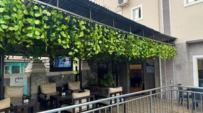 Un espace extérieur aménagé avec des tables et des chaises, un écran de télévision et un mur recouvert de verdure.
