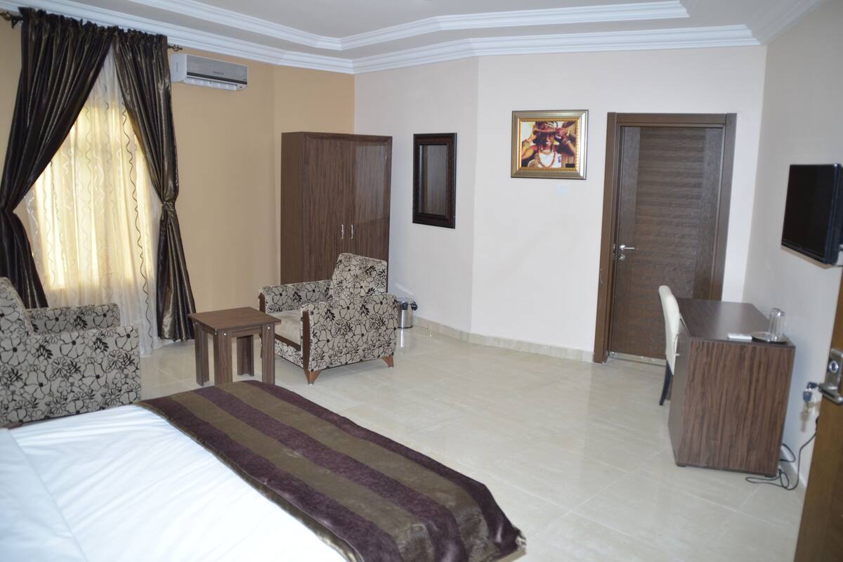 A hotel room with a bed, a desk, a chair, a wardrobe, and a television.