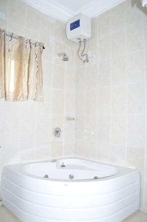 Une salle de bain dotée d’une grande baignoire, d’une douche et d’un chauffe-eau fixé au mur.
