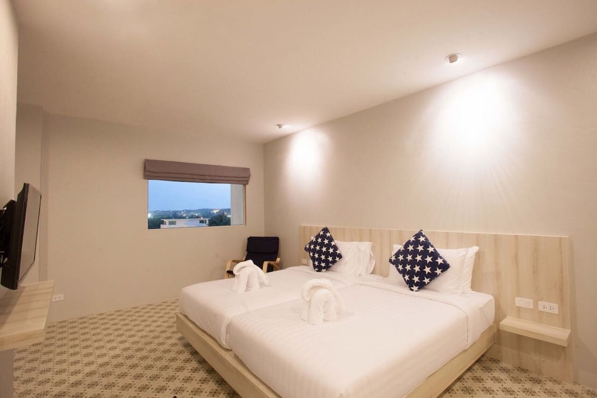A hotel room with a large bed, a small window, a chair, and a TV.