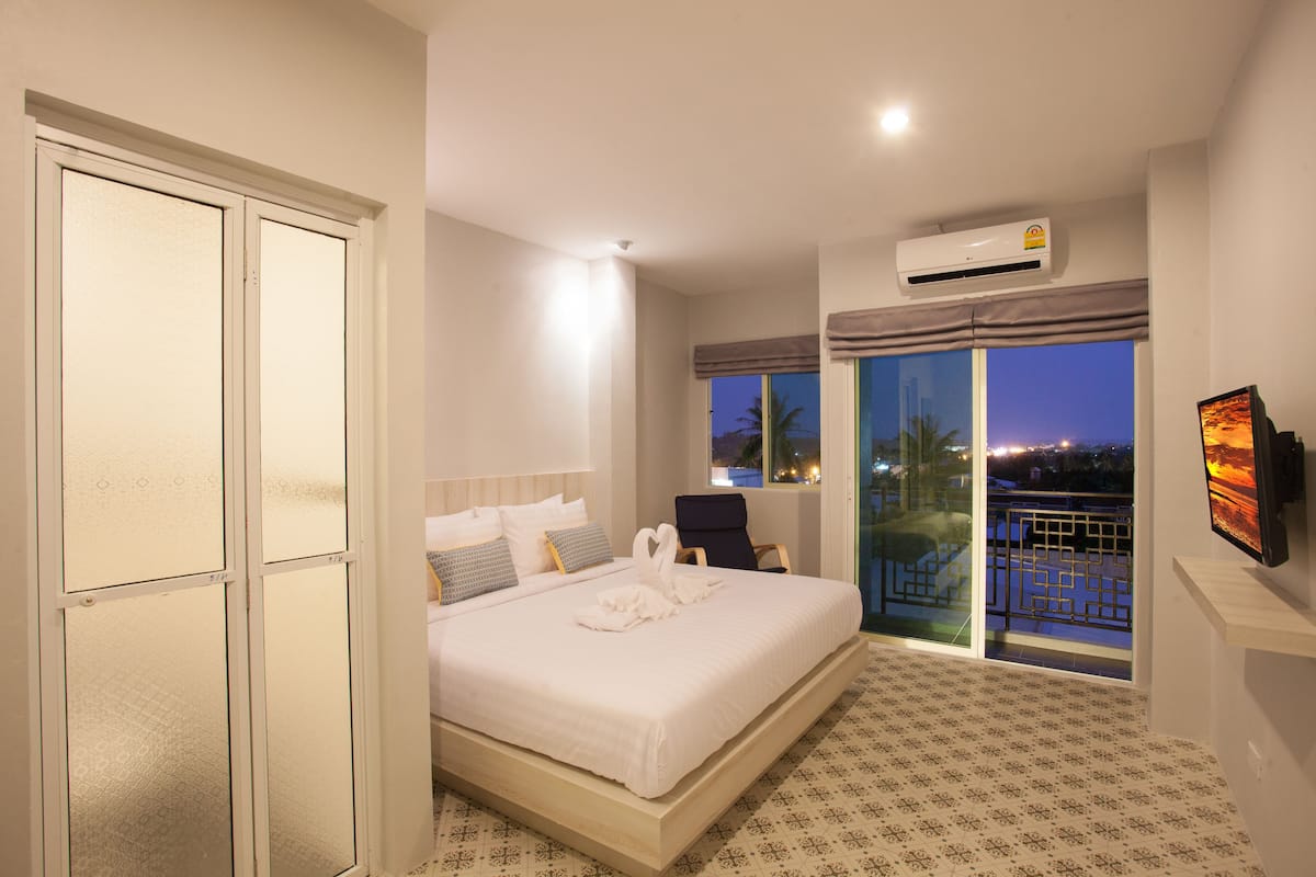 A hotel room with a bed, a chair, a TV, and a balcony with a view of the city at night.