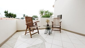 Varanda com duas cadeiras de madeira e uma mesa pequena com um vaso de flores.