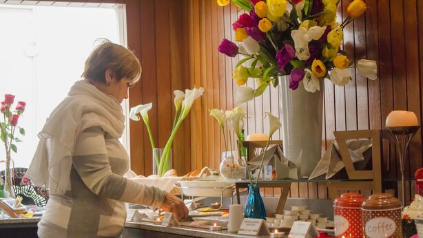 Uma pessoa organizando objetos em um balcão, com um vaso de flores e potes rotulados como 'café' e 'chá' ao fundo.