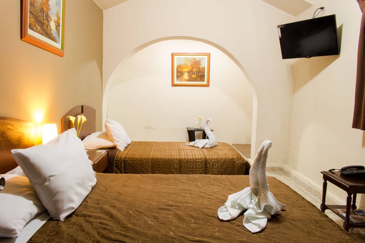 Ein Hotelzimmer mit zwei Betten, einem an der Wand befestigten Fernseher und einem Bild über den Betten.