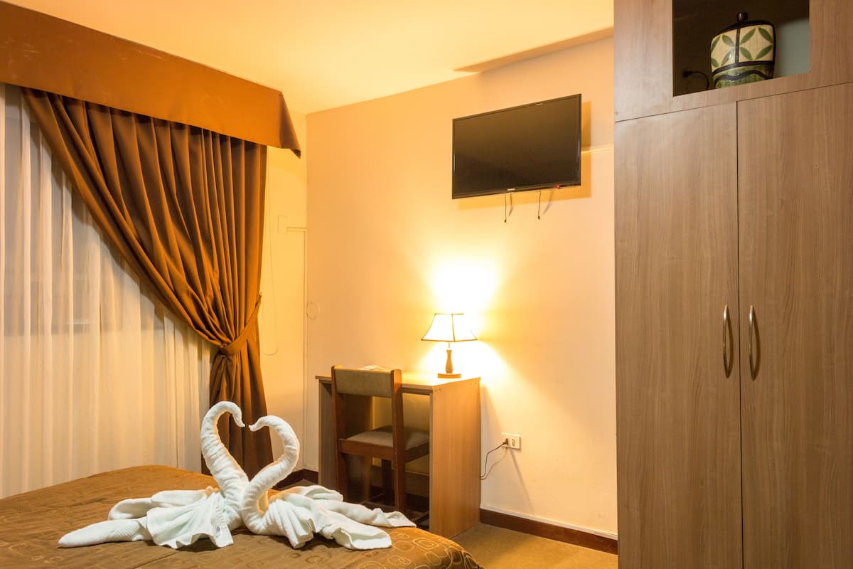 Ein Hotelzimmer mit einem Bett, einem Schreibtisch mit Lampe, einem Fernseher an der Wand und einem Kleiderschrank.