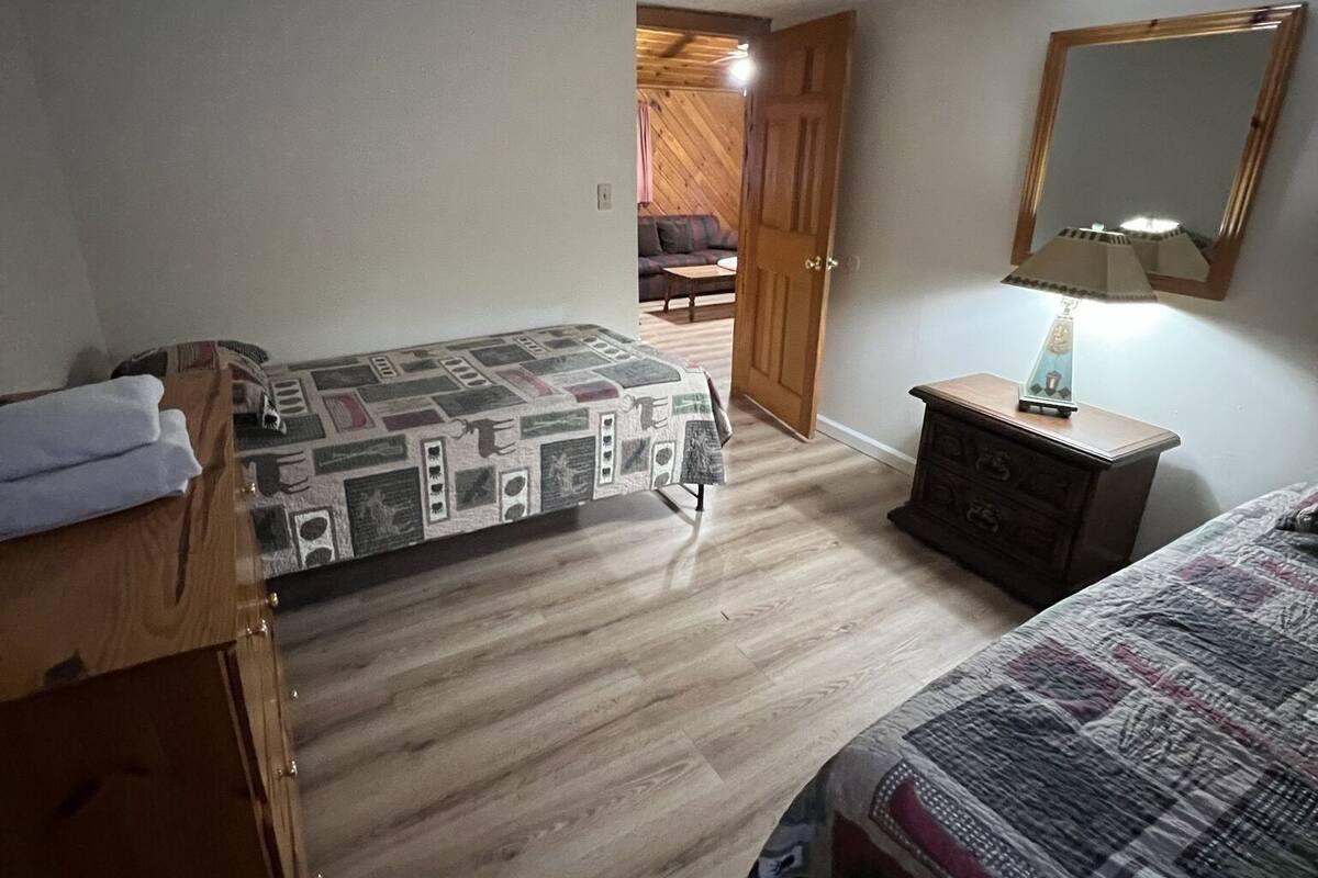 A bedroom with a bed, a dresser, a nightstand, a mirror, and a door leading to another room.