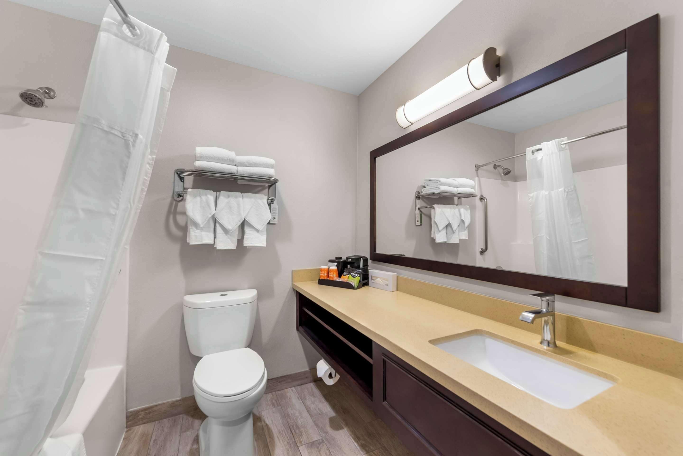 A modern bathroom with a toilet, sink, and shower. There are towels on a rack and a mirror above the sink.