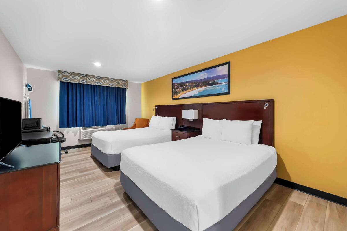 Une chambre d’hôtel avec deux lits, un bureau, une télévision et un tableau représentant une scène de plage.