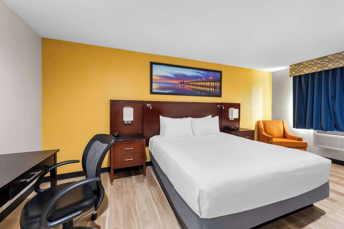 Une chambre d’hôtel avec un grand lit, un bureau, une chaise et un tableau au mur.