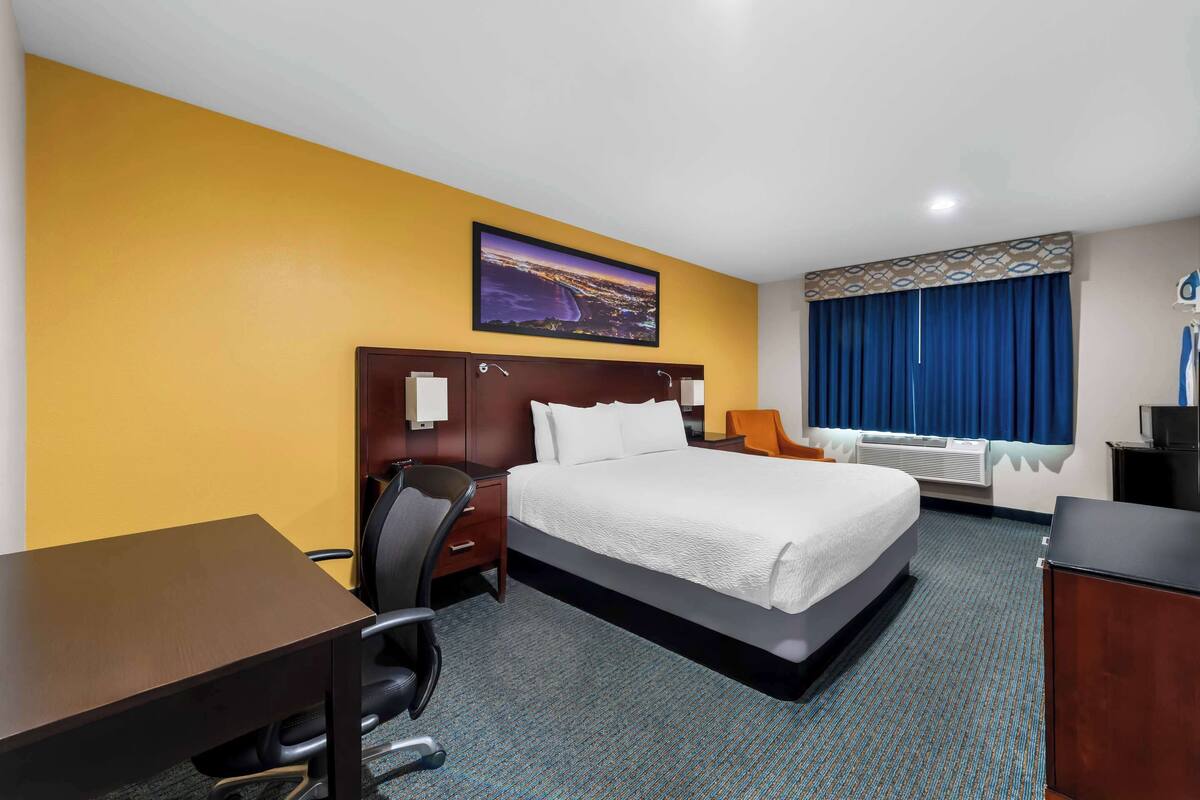 Une chambre d’hôtel avec un lit, un bureau, une chaise et une grande fenêtre avec des rideaux.