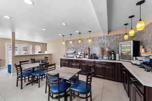 A modern kitchen with a herringbone-patterned backsplash, a central island with a coffee machine, and pendant lighting. - Quality Inn San Diego South - Chula Vista (Chula Vista)
