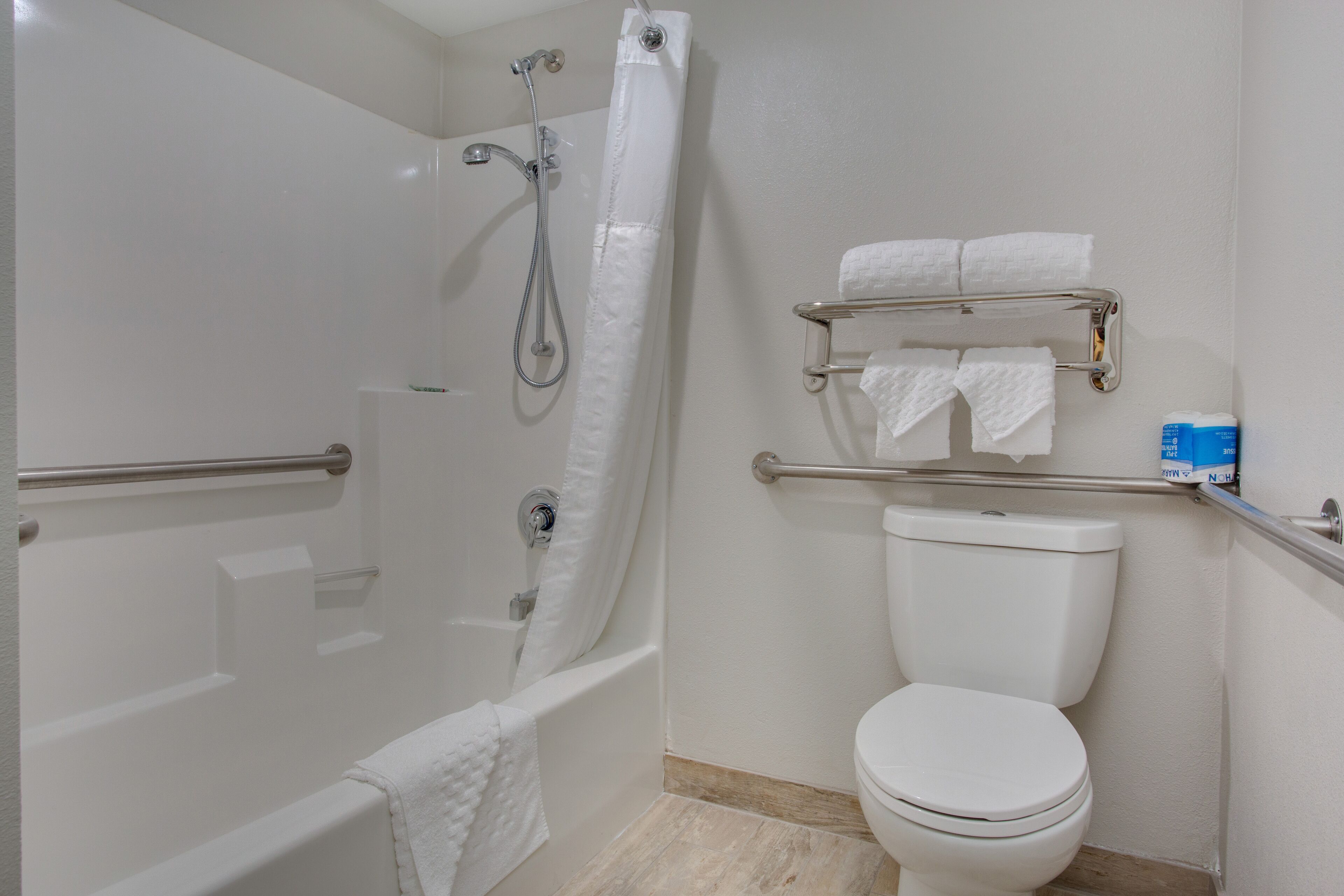 Ein modernes Badezimmer mit barrierefreier Dusche, Haltegriffen, Toilette und Handtuchhalter.