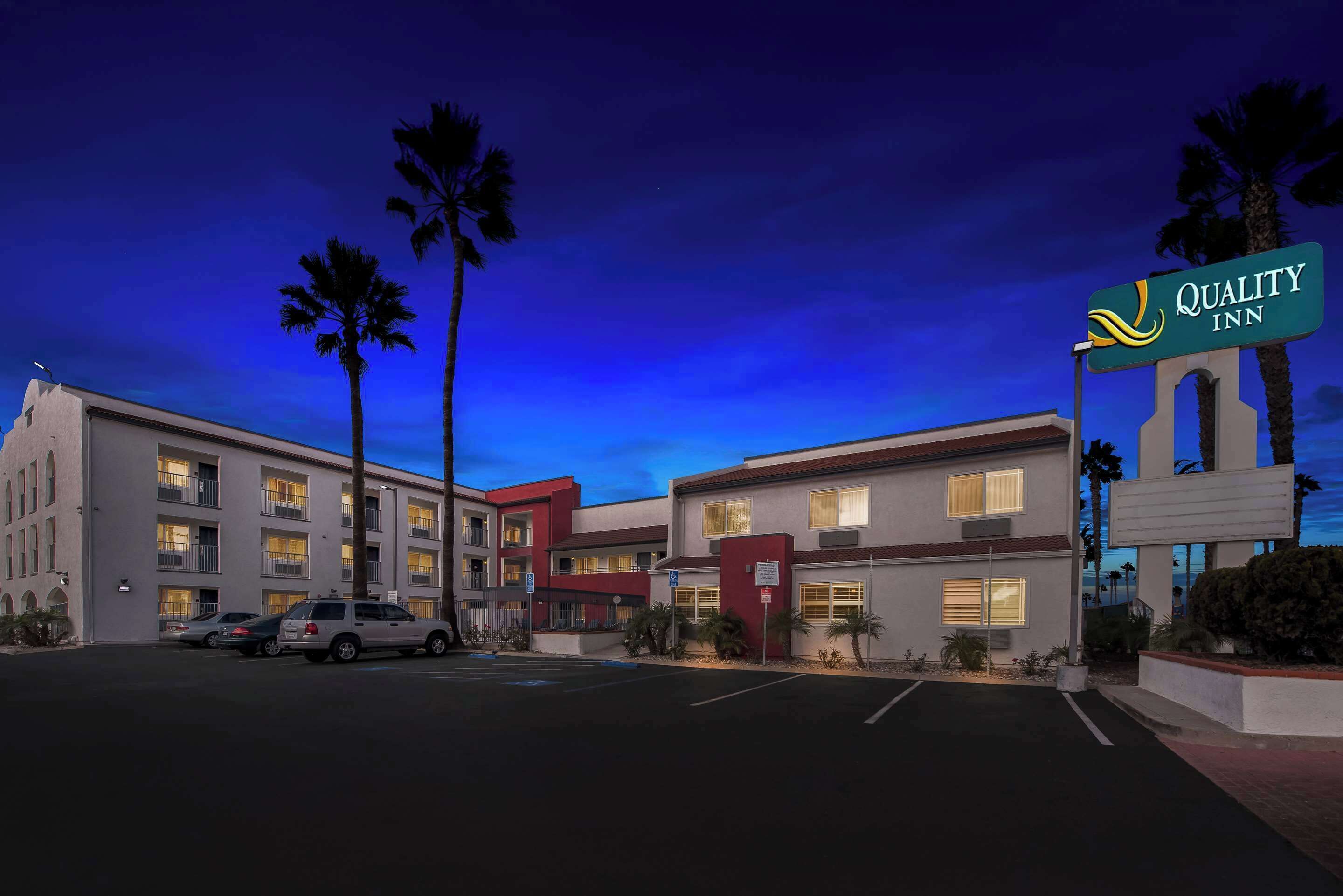 Un hotel de varios pisos con un cartel llamativo de Quality Inn, que presenta un diseño arquitectónico moderno con balcones y un estacionamiento al frente.