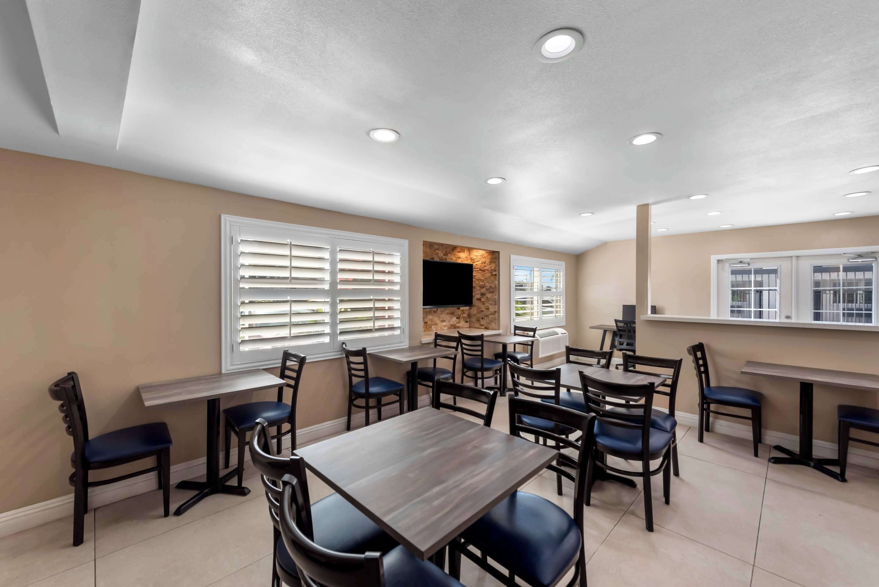 A dining area with multiple tables and chairs, a stone accent wall, and a flat-screen TV mounted above a fireplace.