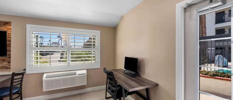 Quarto com escrivaninha, cadeira e janela com persianas.