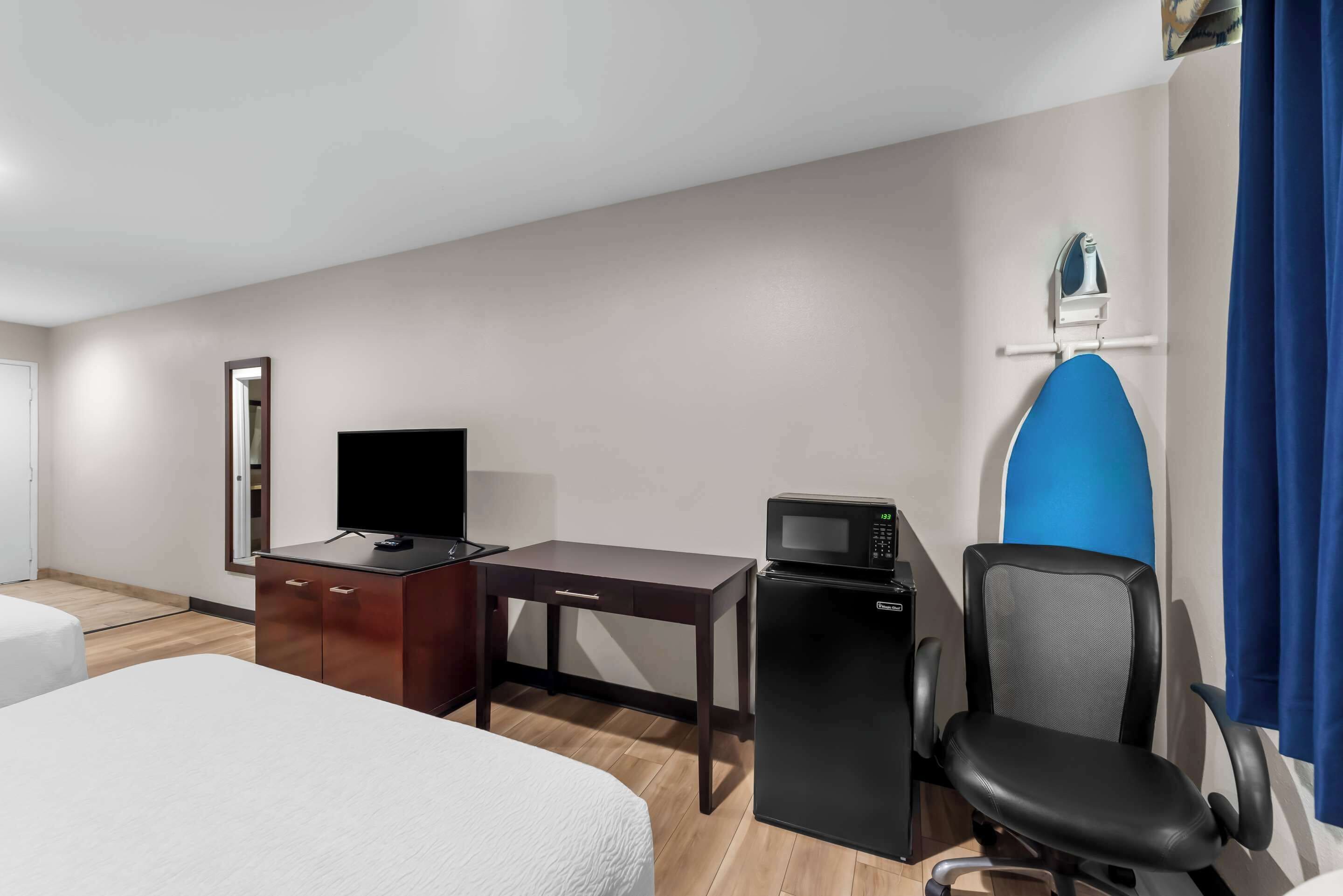 Habitación de hotel con cama, escritorio, computadora, microondas y una silla.
