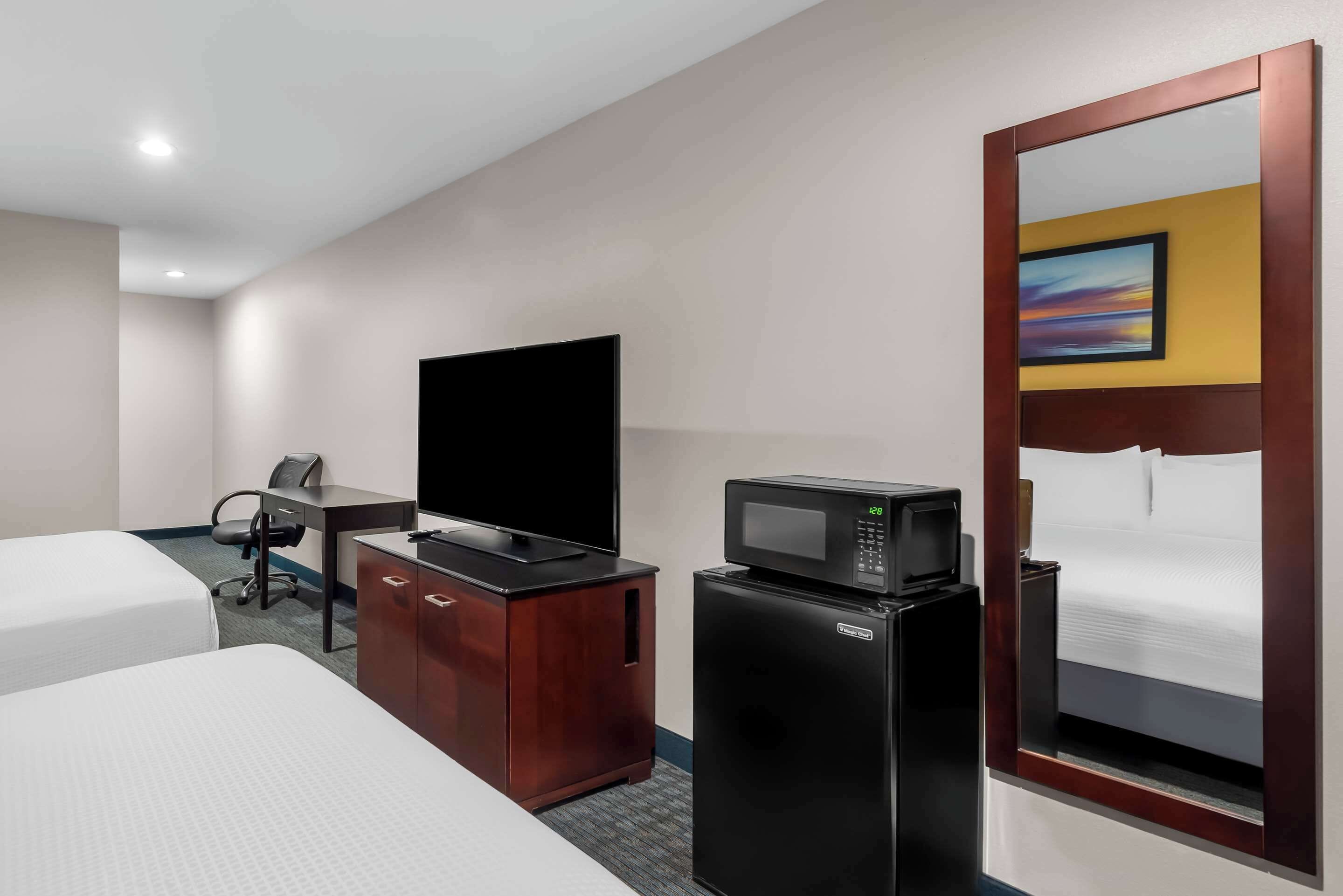 Une chambre d’hôtel avec deux lits, un bureau avec une chaise, une télévision, un four à micro-ondes et un réfrigérateur.