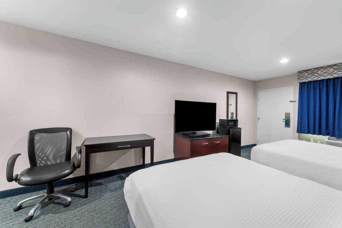 Une chambre d’hôtel avec un lit, un bureau avec un ordinateur, une chaise, une télévision et une porte avec des rideaux.